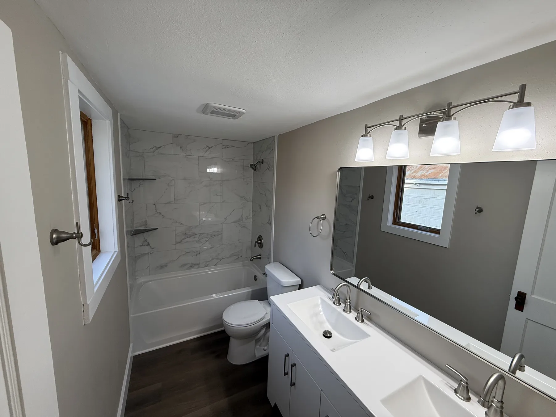 Renovated bathroom with a marble-look tile tub surround, a white double vanity and brushed nickel fixtures, by NextGen Bathroom Specialists