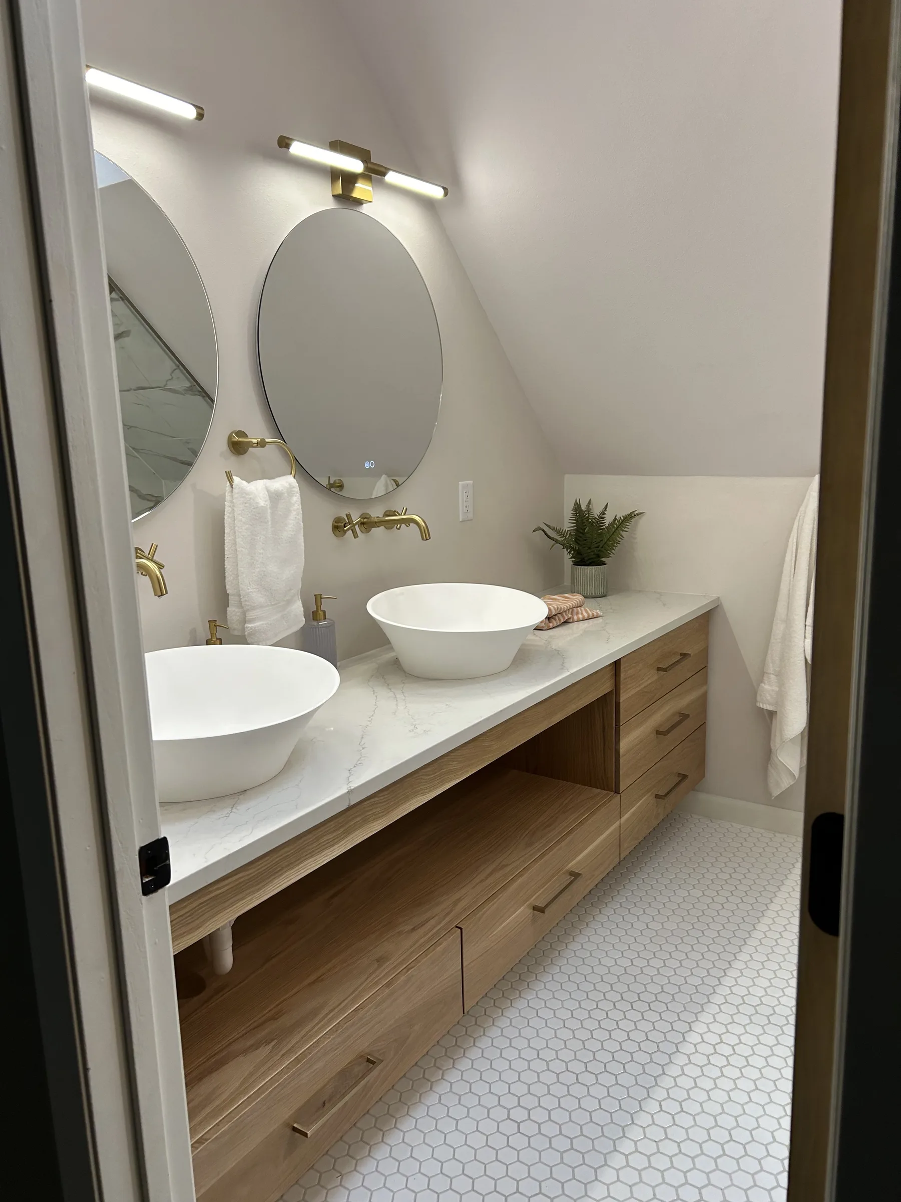 Double vessel-sink vanity in white oak with a quartz counter, brass wall-mounted faucets and round mirrors, completed by NextGen Bathroom Specialists